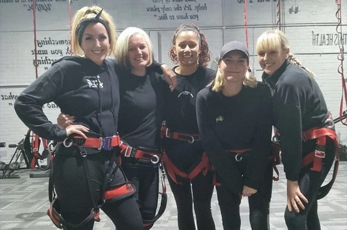 Group of five women wearing harnesses, ready for an indoor climbing experience.